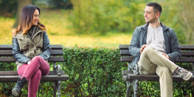A man & woman sitting on separate park benches chatting