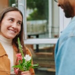 A woman smiling at a man with flowers in her hands.