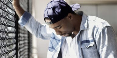 A guy standing against a fence looking upset