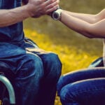 A couple in each in wheelchairs holding each other's hands