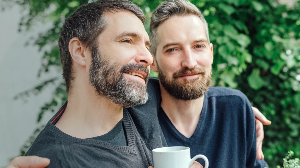 A gay couple enjoying a cup of coffee outdoors together.