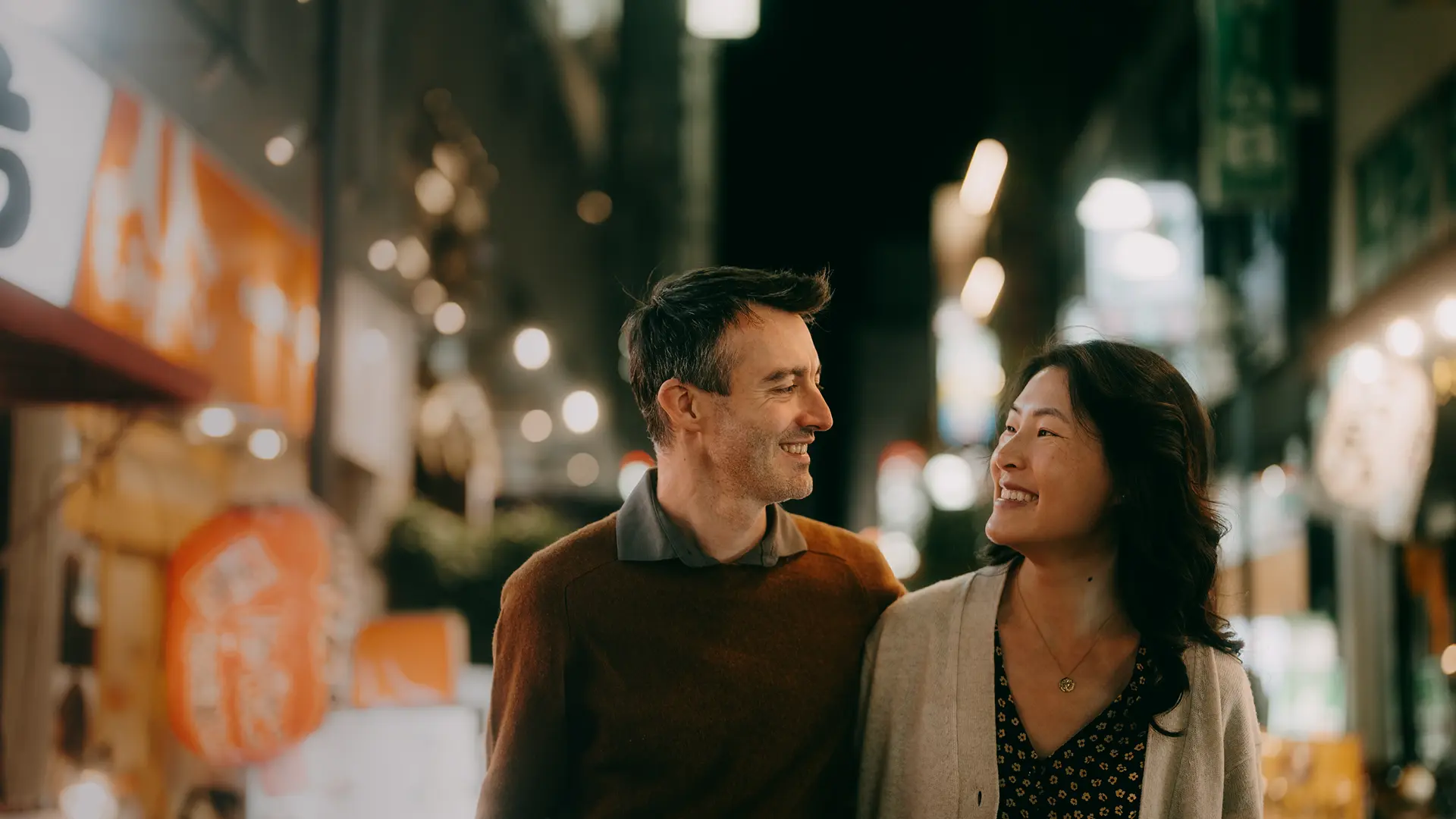 A japanese couple is walking on the street at night time.